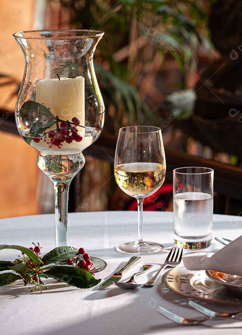 Mesa bistrô decorada com prato e talheres, vela, taça de vinho de cristal e taça de água. fundo desfocado.