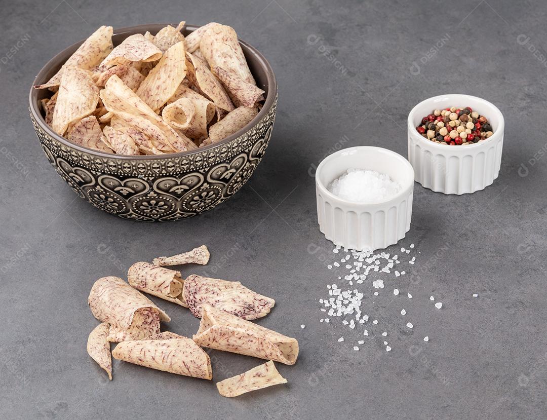 Yam or taro chips in bowl with raw vegetables on stone