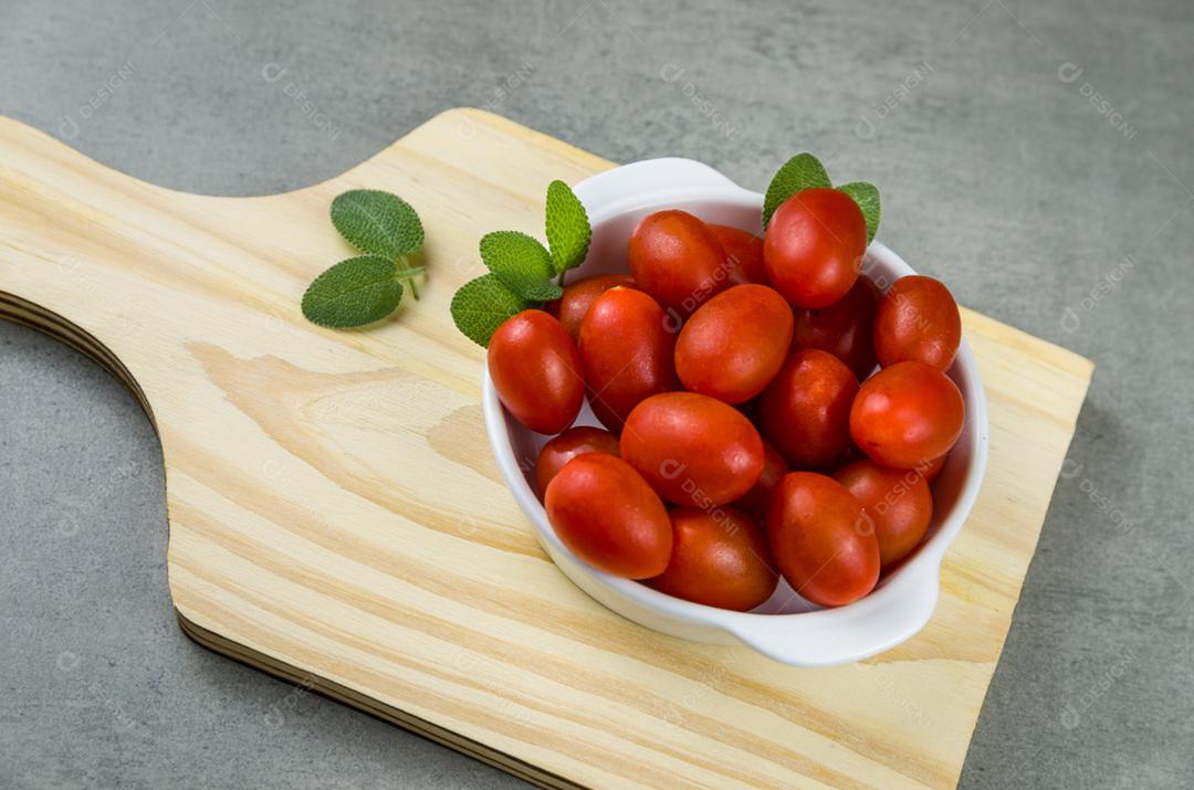 Placa de madeira com tomate cereja em fundo cinza. fundo culinário.