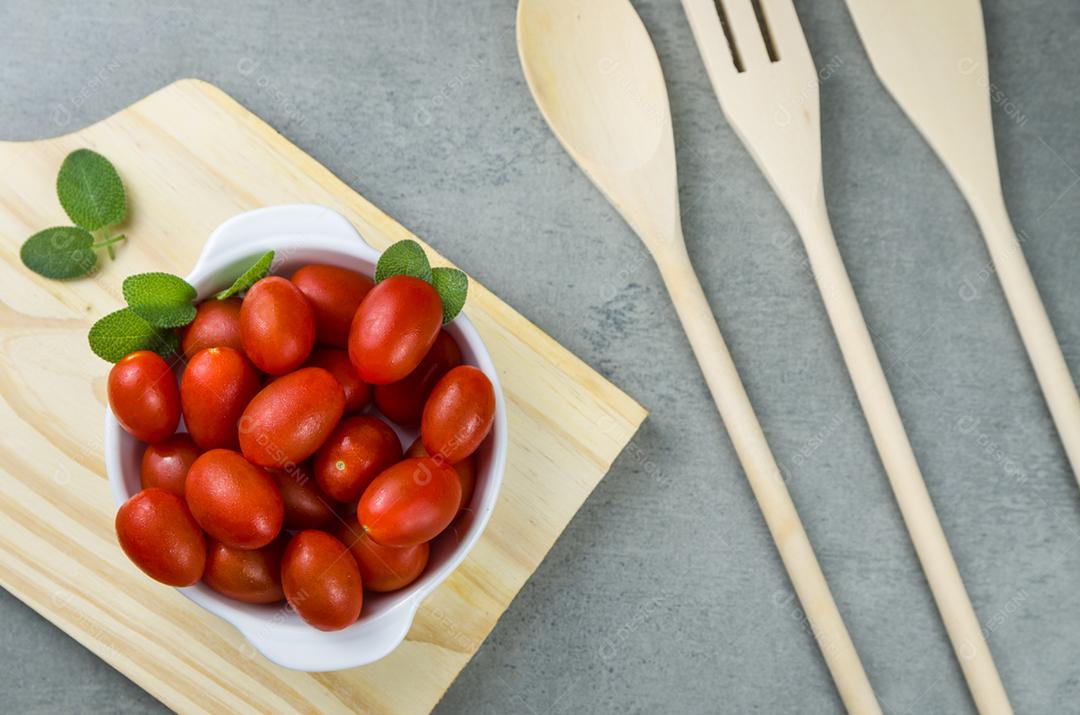 Placa de madeira com tomate cereja em fundo cinza. fundo culinário.