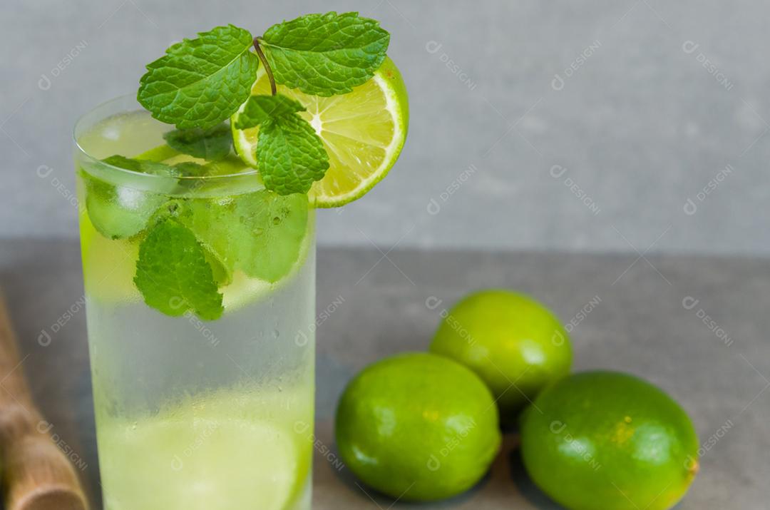 Copo de coquetel de mojito com hortelã e limão em um fundo cinza de concreto com limão fresco