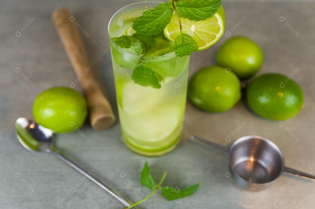 Copo de coquetel de mojito com hortelã e limão em um fundo cinza de concreto com limão fresco