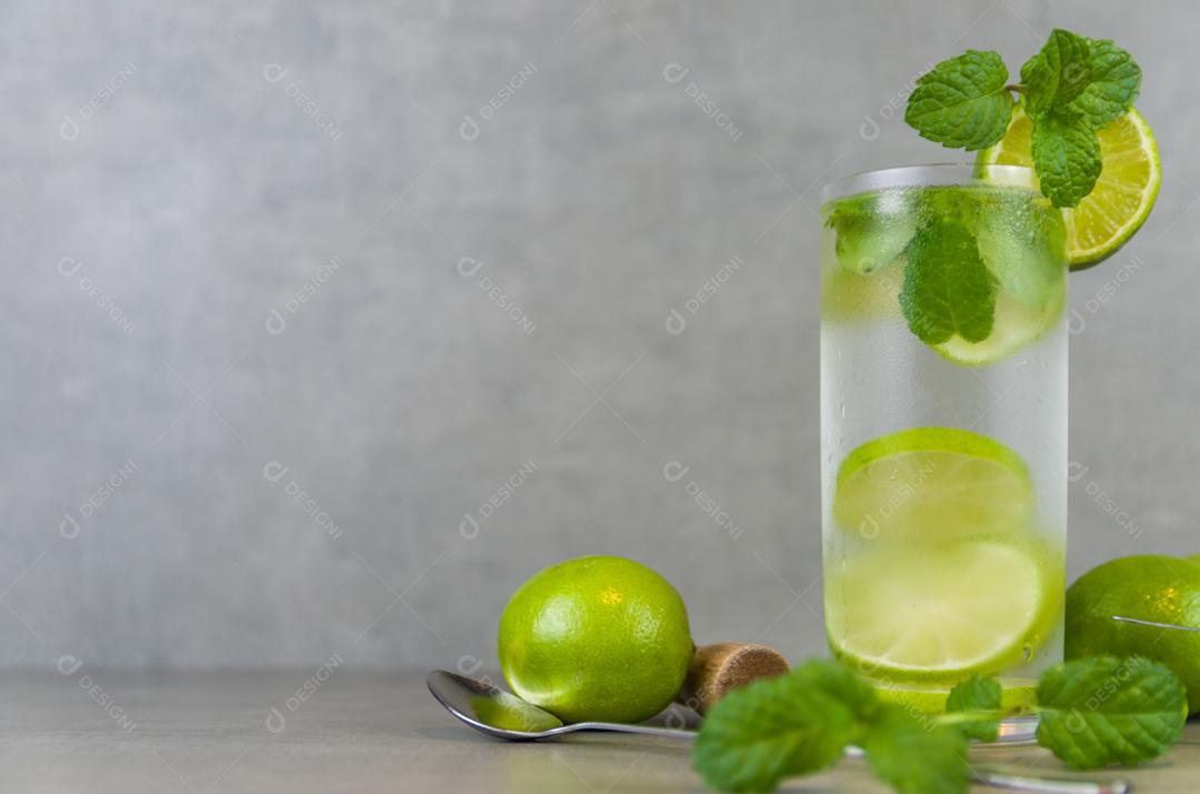 Copo de coquetel de mojito com hortelã e limão em um fundo cinza de concreto com limão fresco