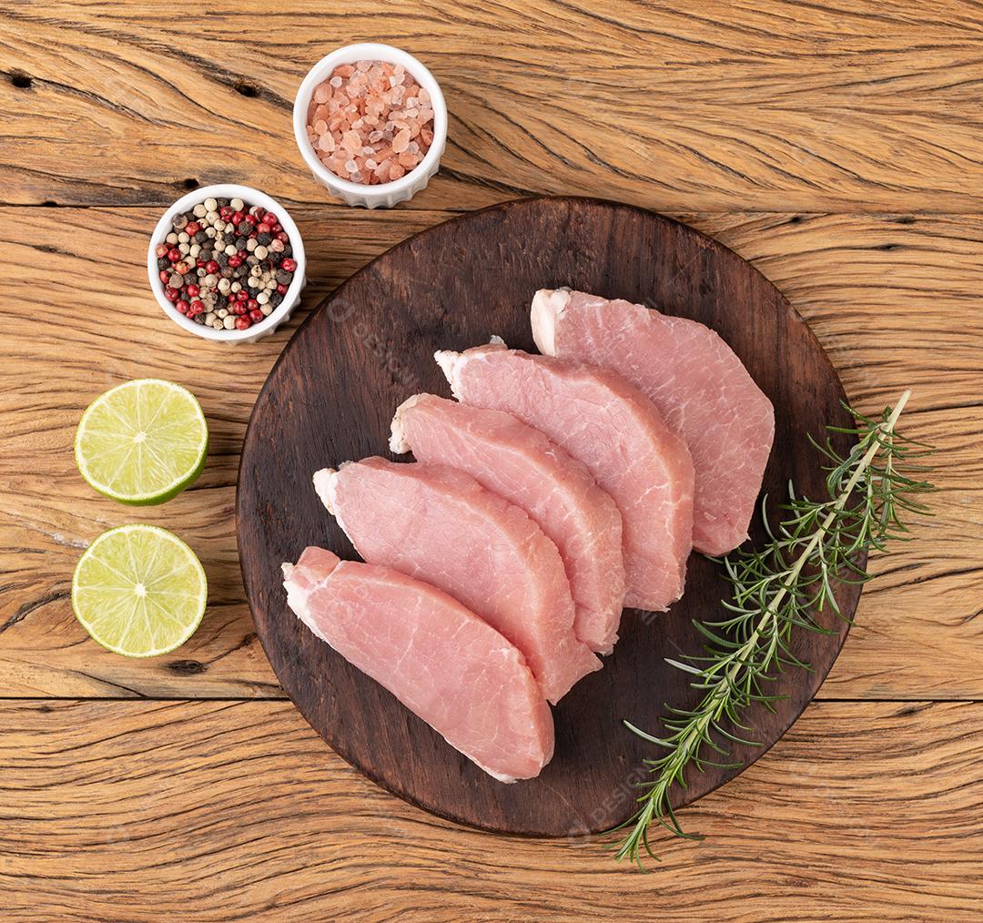 Carne de lombo de porco crua fatiada sobre tábua de madeira com temperos