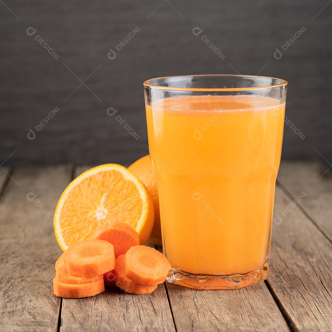 Suco de laranja e cenoura em um copo com frutas sobre mesa de madeira