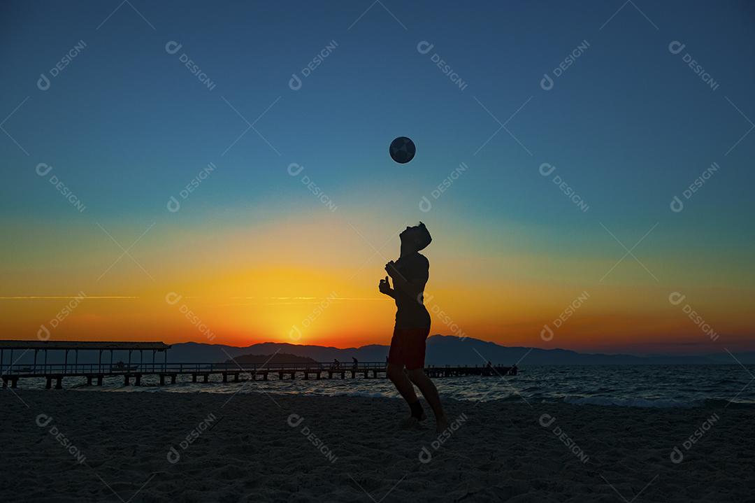 Homem jogando bola em praia com por do sol lindo. Esporte. Futebol