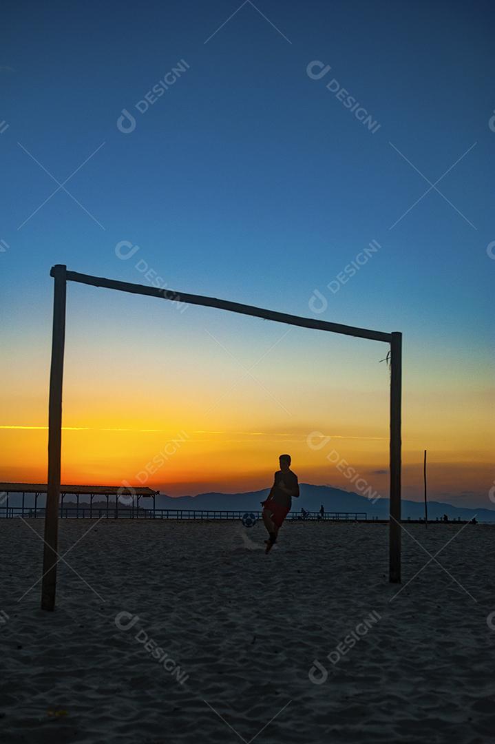 Homem jogando bola em praia com por do sol lindo. Esporte. Futebol
