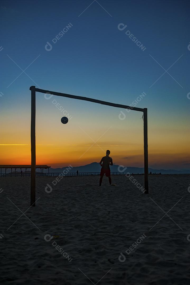 Homem jogando bola em praia com por do sol lindo. Esporte. Futebol