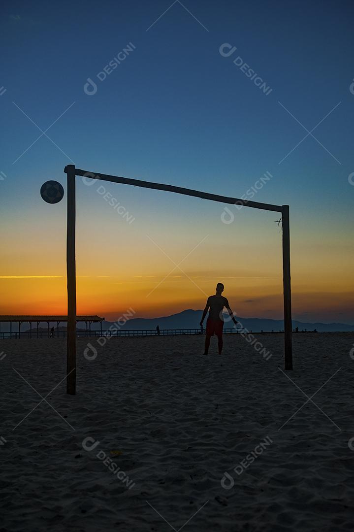 Homem jogando bola em praia com por do sol lindo. Esporte. Futebol