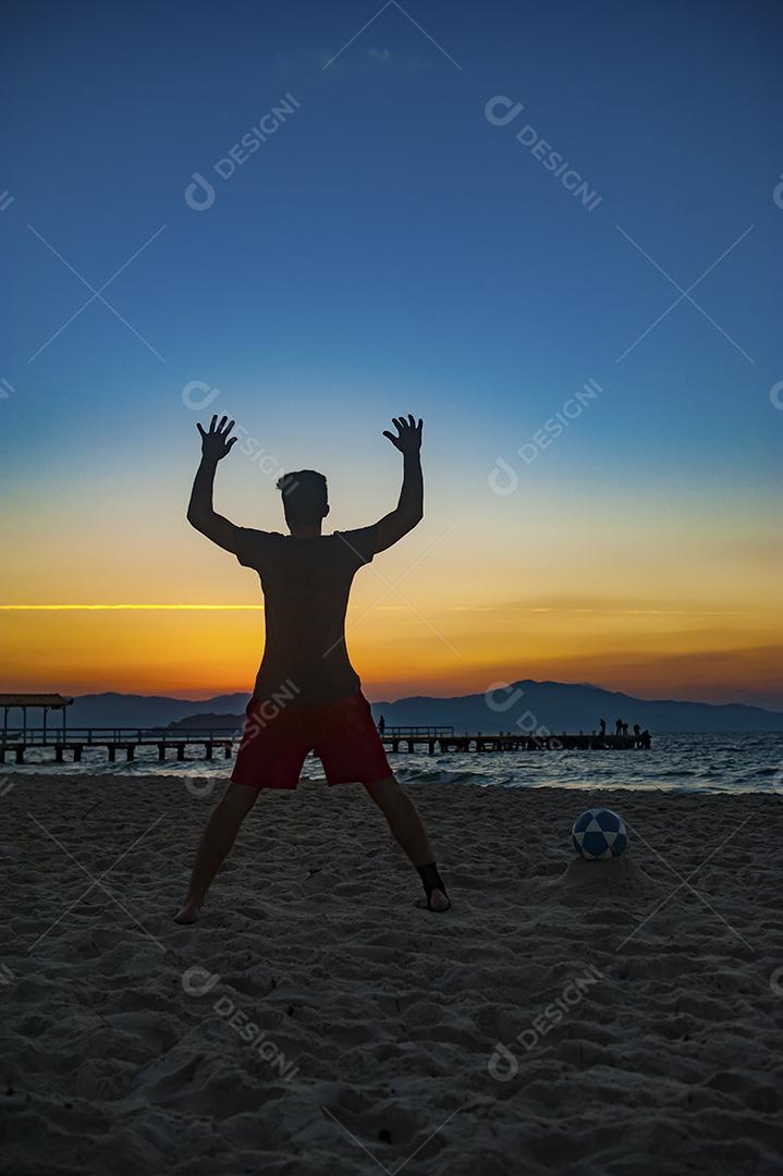 Homem jogando bola em praia com por do sol lindo. Esporte. Futebol