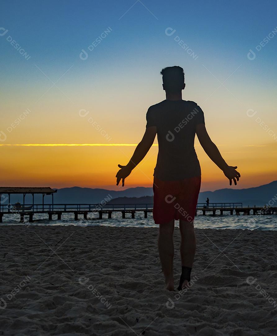 Atleta latino alegre olhando horizonte ao por do sol feliz em praia beira mar