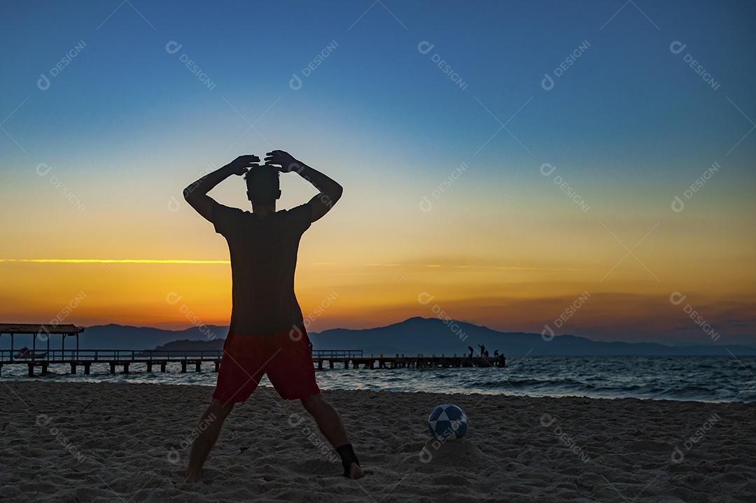 Homem jogando bola em praia com por do sol lindo. Esporte. Futebol