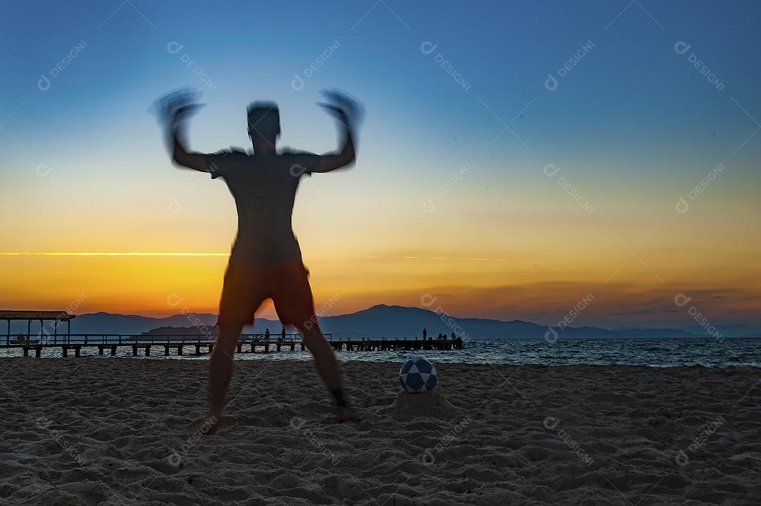 Homem jogando bola em praia com por do sol lindo. Esporte. Futebol