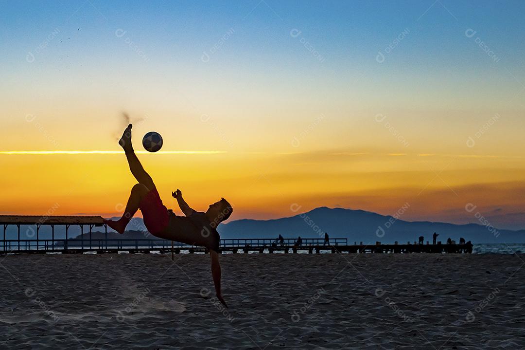 Homem jogando bola em praia com por do sol lindo. Esporte. Futebol