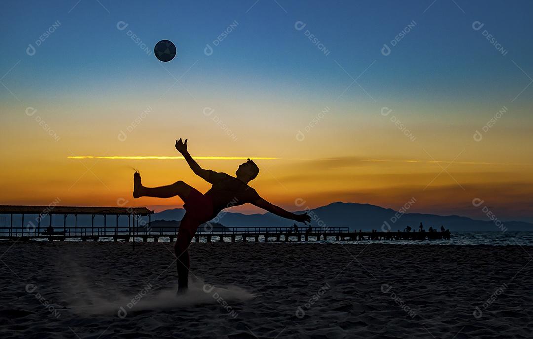 Homem jogando bola em praia com por do sol lindo. Esporte. Futebol