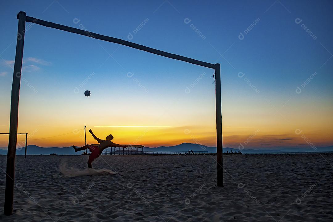 Homem jogando bola em praia com por do sol lindo. Esporte. Futebol