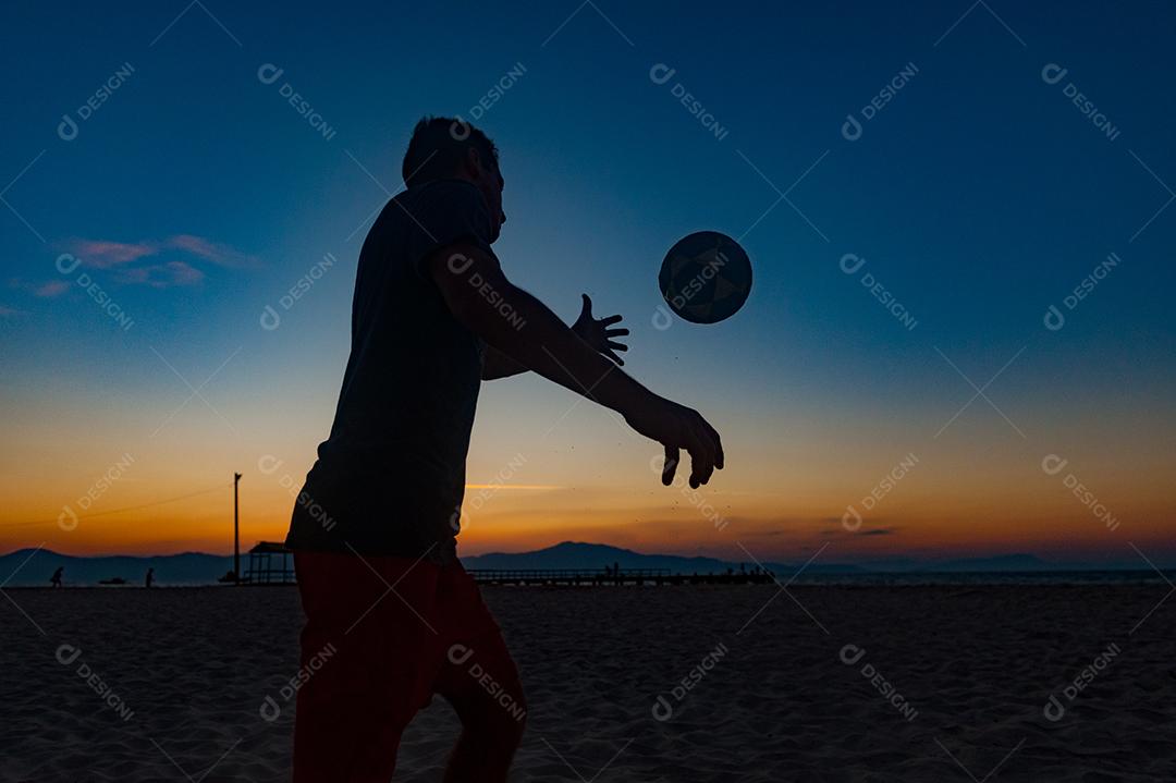 Homem jogando bola em praia com por so sol lindo. Esporte. Futebol