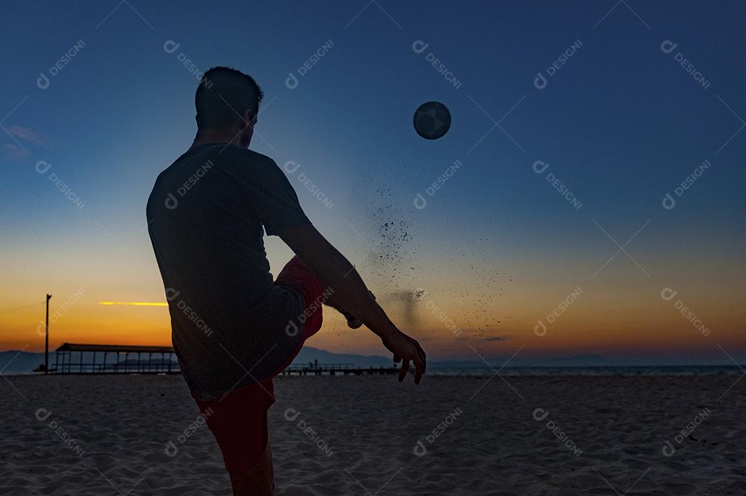 Homem jogando bola em praia com por so sol lindo. Esporte. Futebol