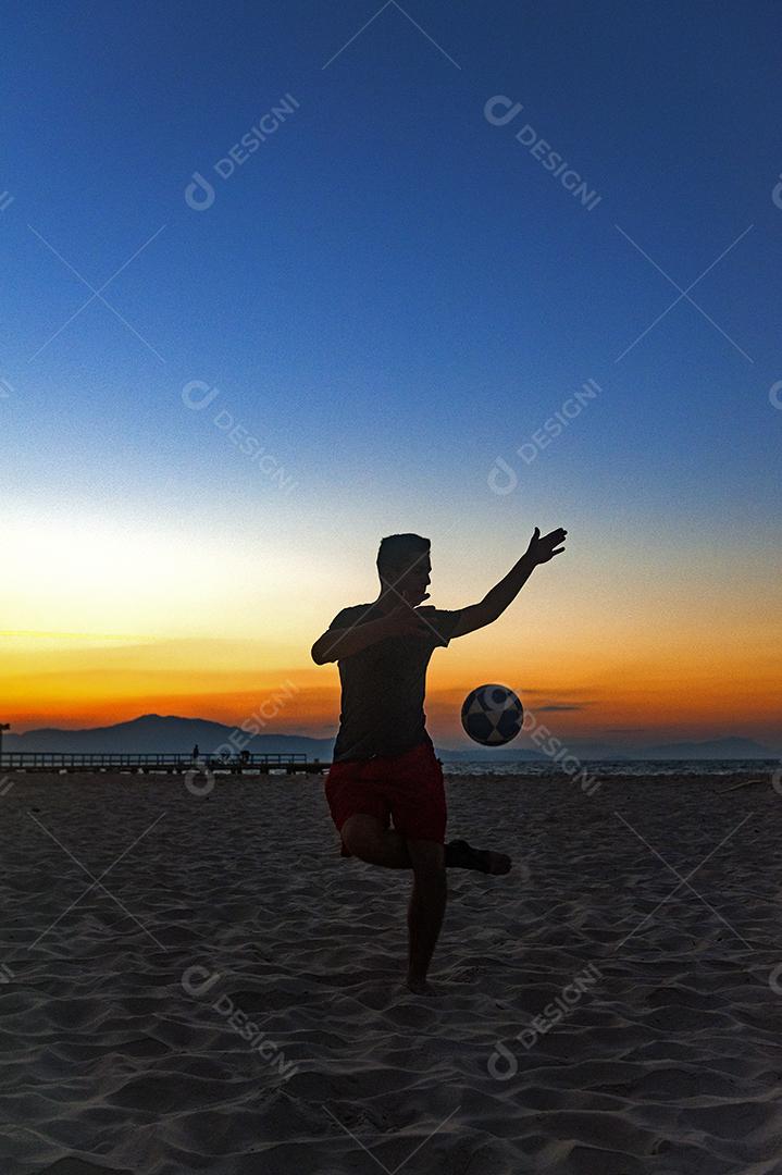 Homem jogando bola em praia com por so sol lindo. Esporte. Futebol