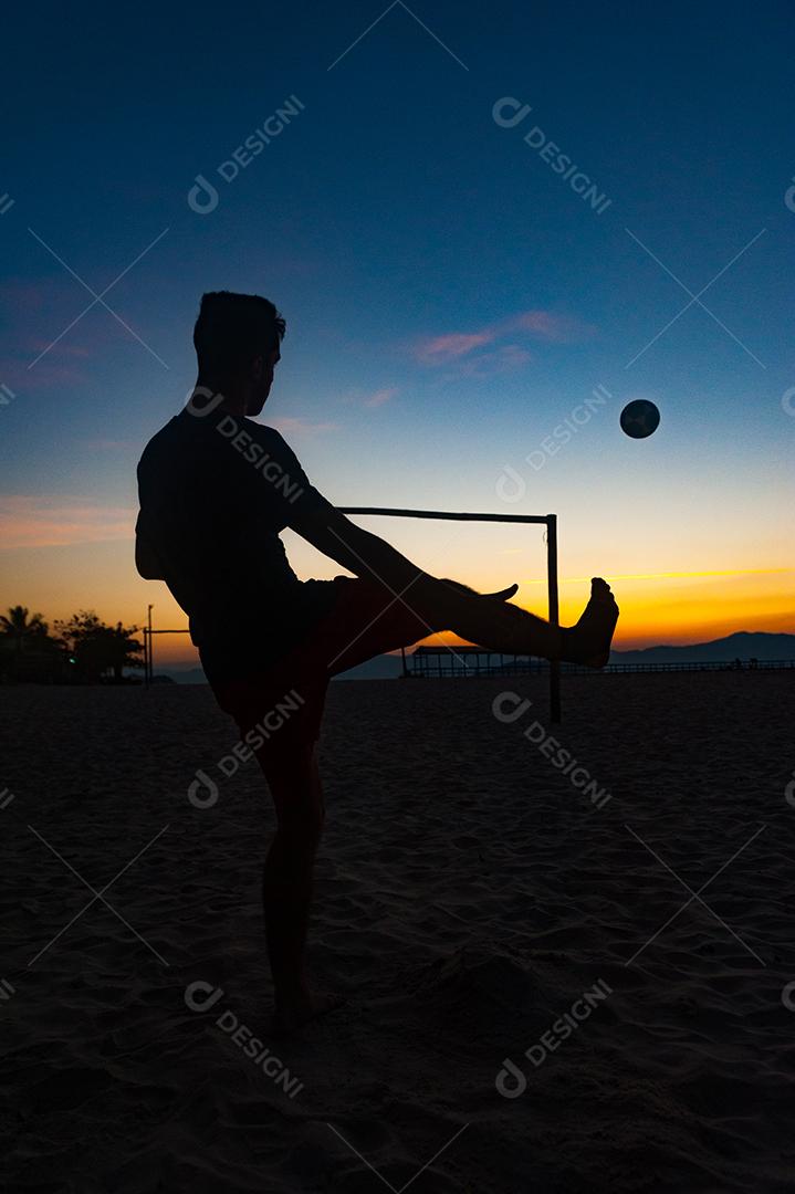 Homem jogando bola em praia com por so sol lindo. Esporte. Futebol