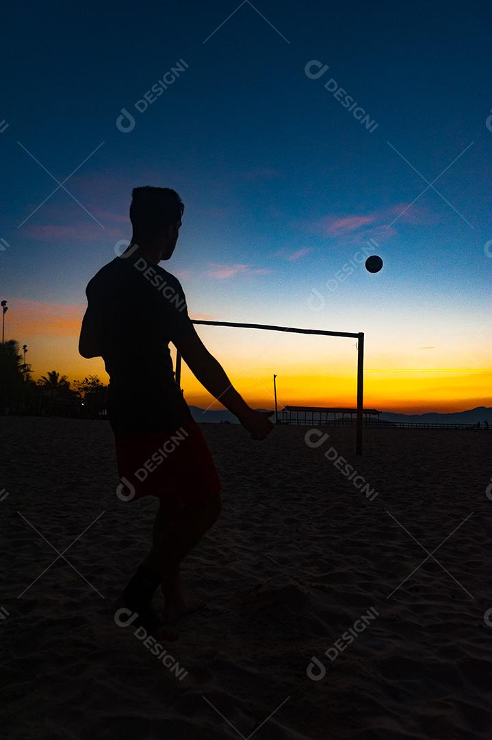 Homem jogando bola em praia com por so sol lindo. Esporte. Futebol