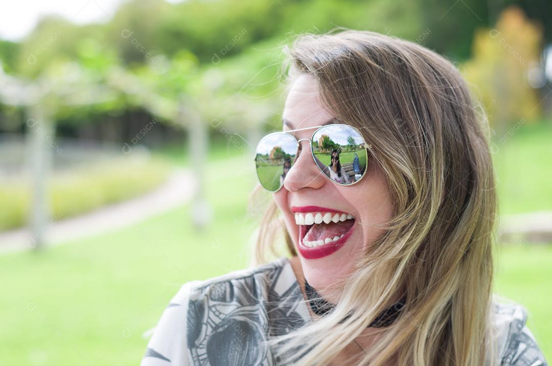 Jovem mulher loira feliz rindo no gramado.