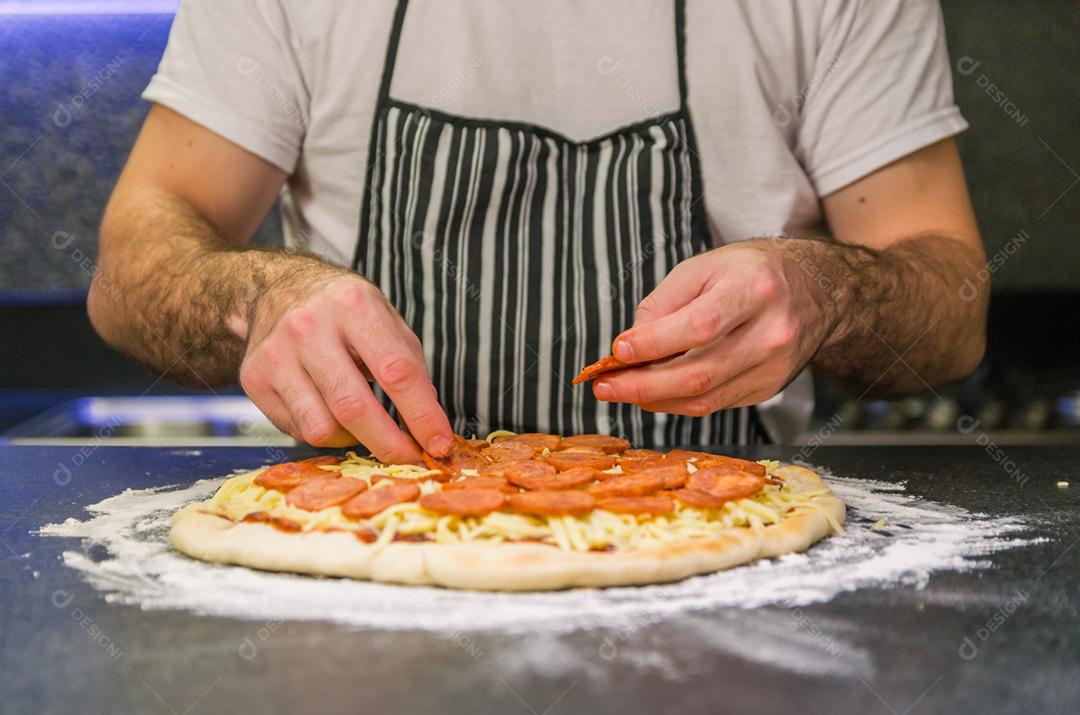 Homem preparando pizza de calabresa na mesa de granito preto