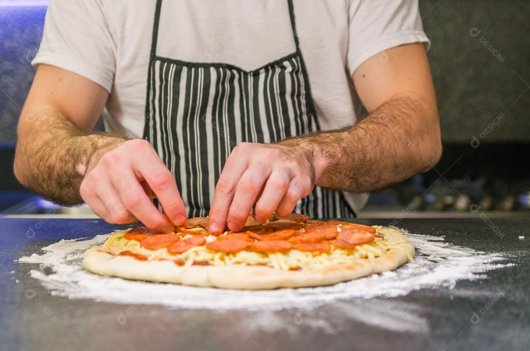 Homem preparando pizza de calabresa na mesa de granito preto