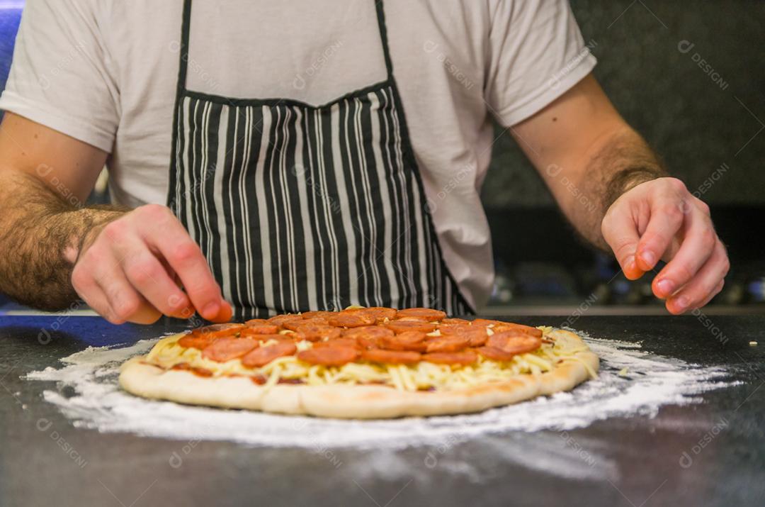Homem preparando pizza de calabresa na mesa de granito preto