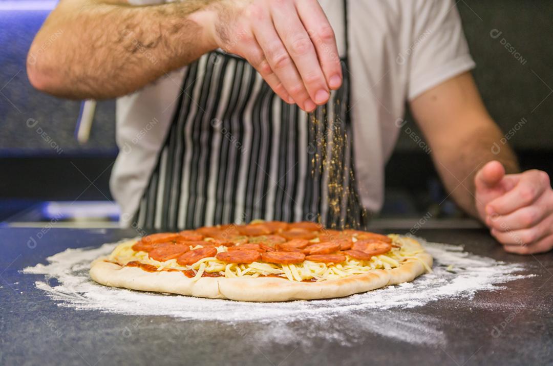 Homem preparando pizza de calabresa na mesa de granito preto