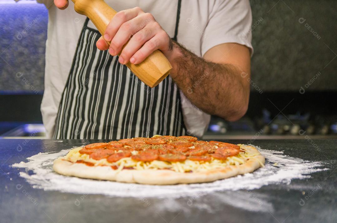 Homem preparando pizza de calabresa na mesa de granito preto