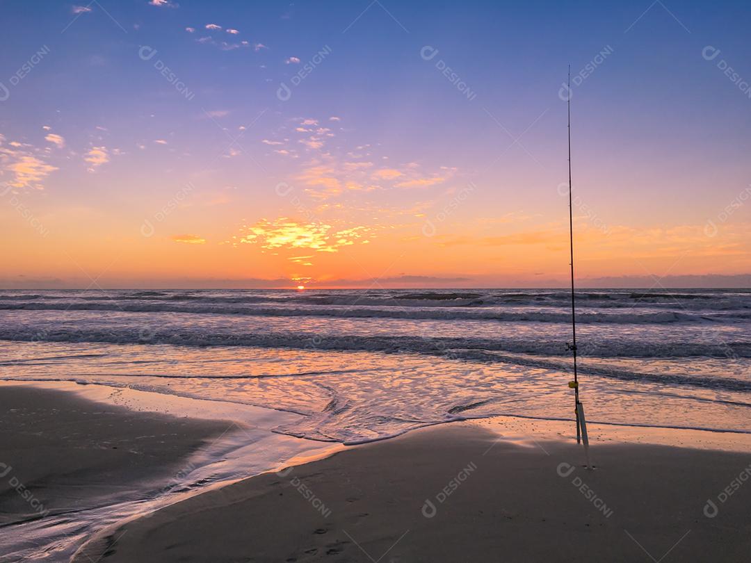 Vara de pesca na praia ao pôr do sol, elenco de surf.