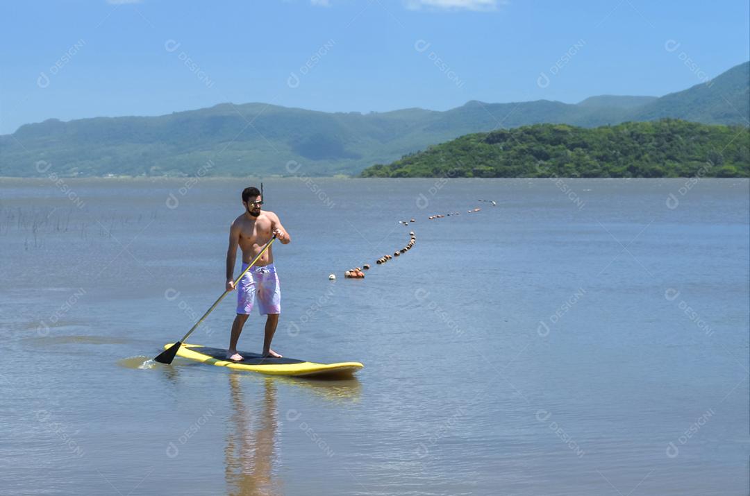 Jovem praticando Stand Up Paddle no lago, placa amarela, remando. Paddleboard.