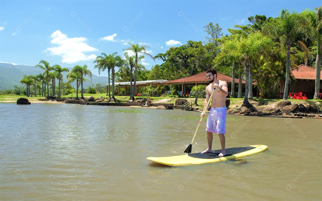 Jovem praticando Stand Up Paddle no lago, placa amarela, remando. Paddleboard.