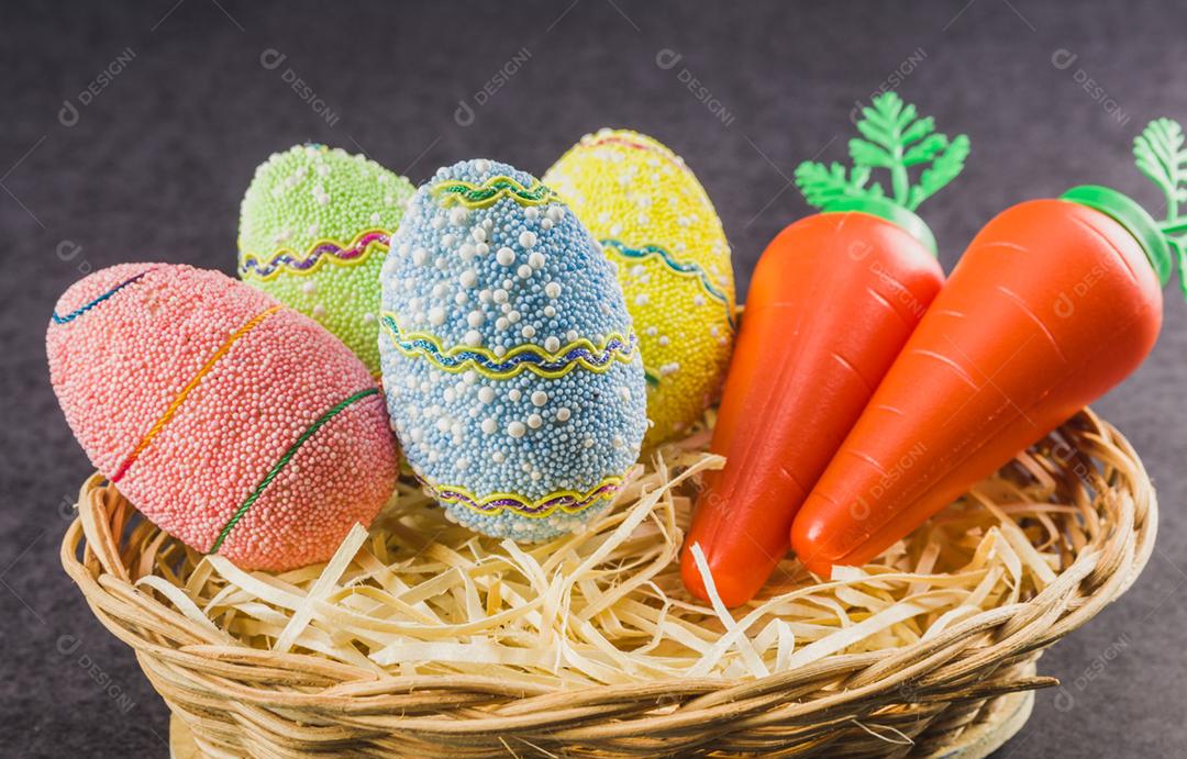 Ovos de Páscoa coloridos e cenouras em uma cesta isolada em um fundo preto na moda. Conceito mínimo de páscoa