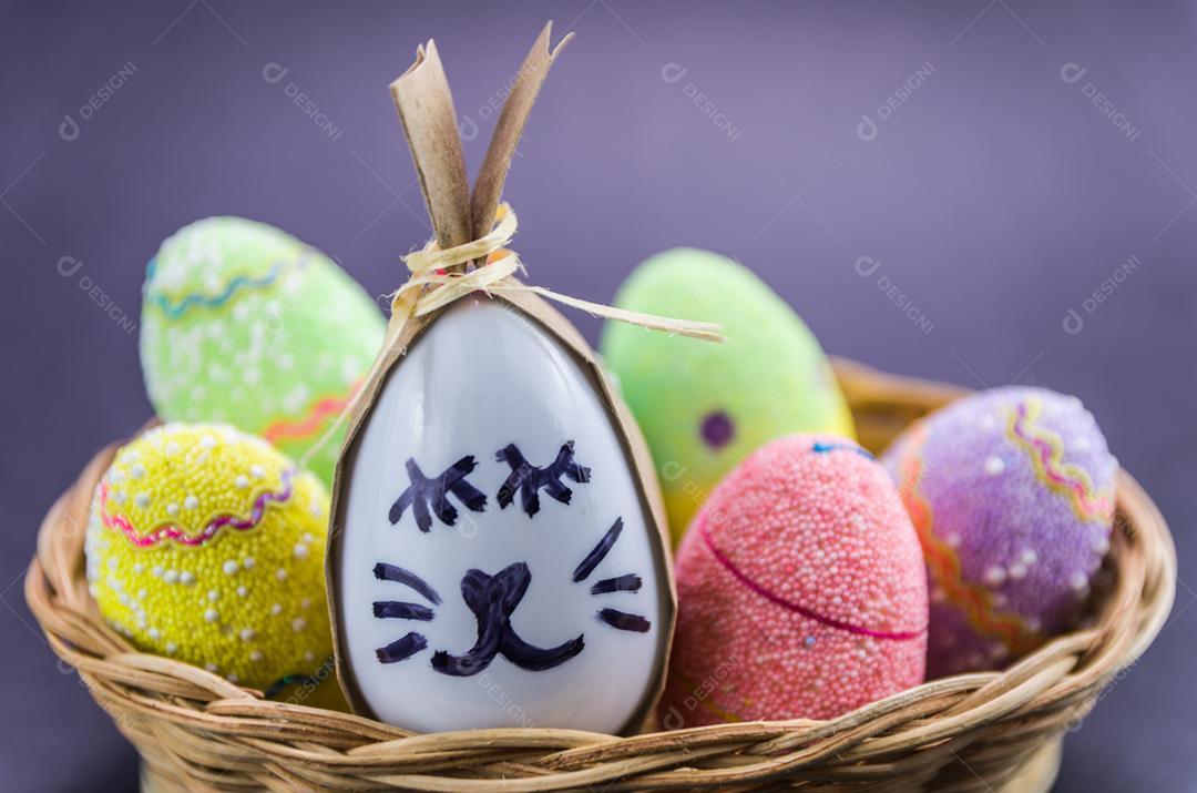 Ovo de coelhinho da páscoa feliz e ovos coloridos em uma cesta isolada em um fundo preto na moda