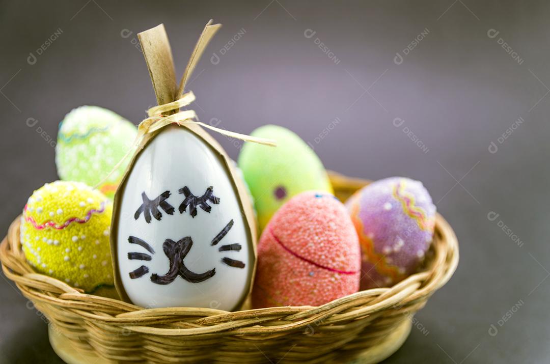 Ovo de coelhinho da páscoa feliz e ovos coloridos em uma cesta isolada em um fundo preto na moda