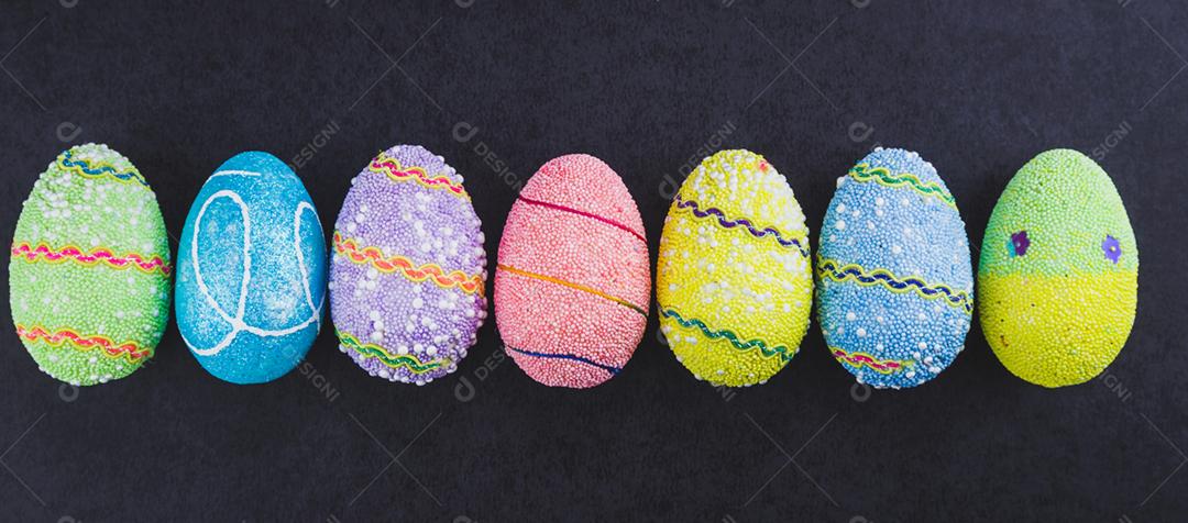 Ovos de Páscoa coloridos alinhados lado a lado em um fundo preto na moda.