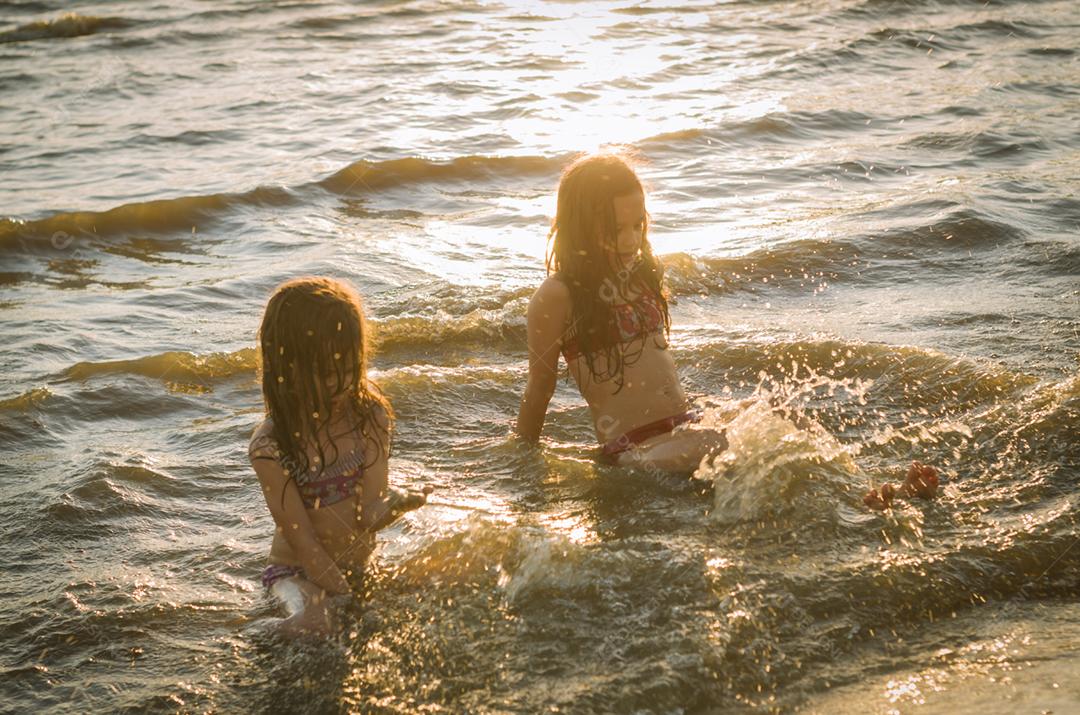 Lindas criança irmãs bricando sobre rio por do sol