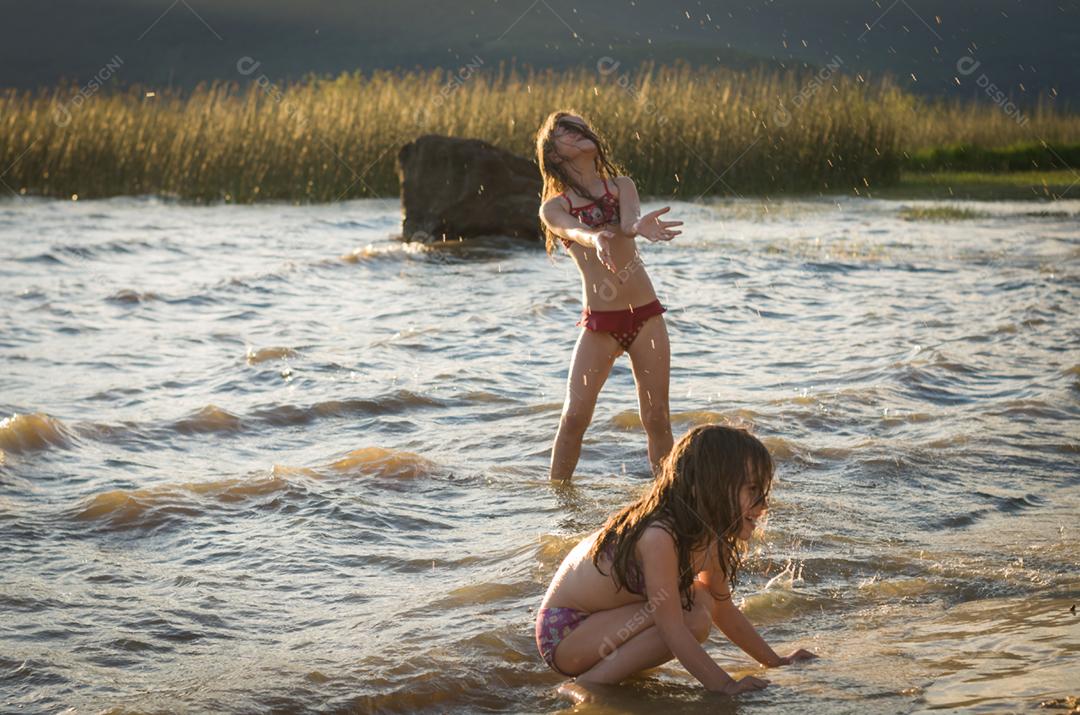 Lindas criança irmãs bricando sobre rio por do sol