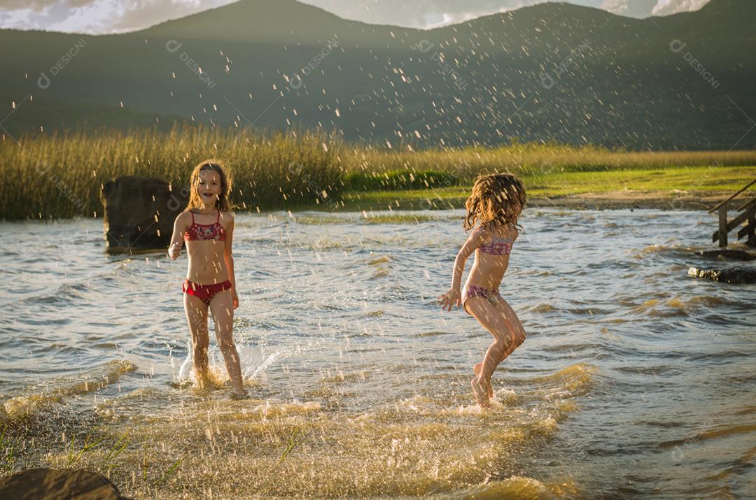 Lindas criança irmãs bricando sobre rio por do sol
