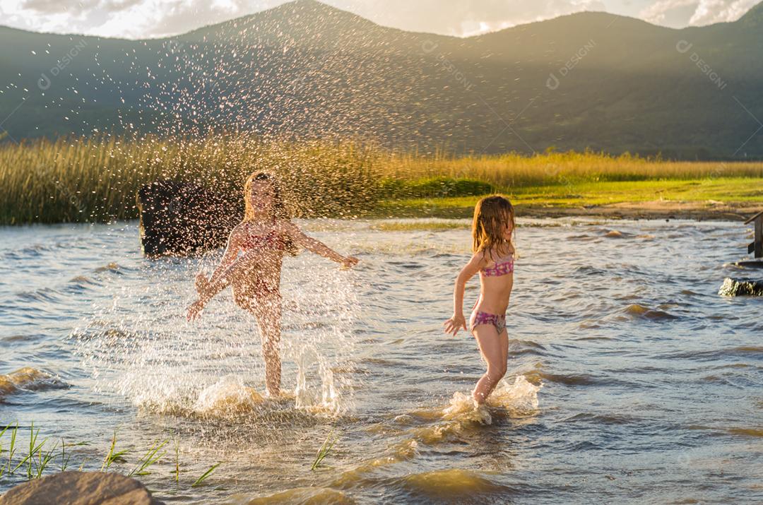 Lindas criança irmãs bricando sobre rio por do sol
