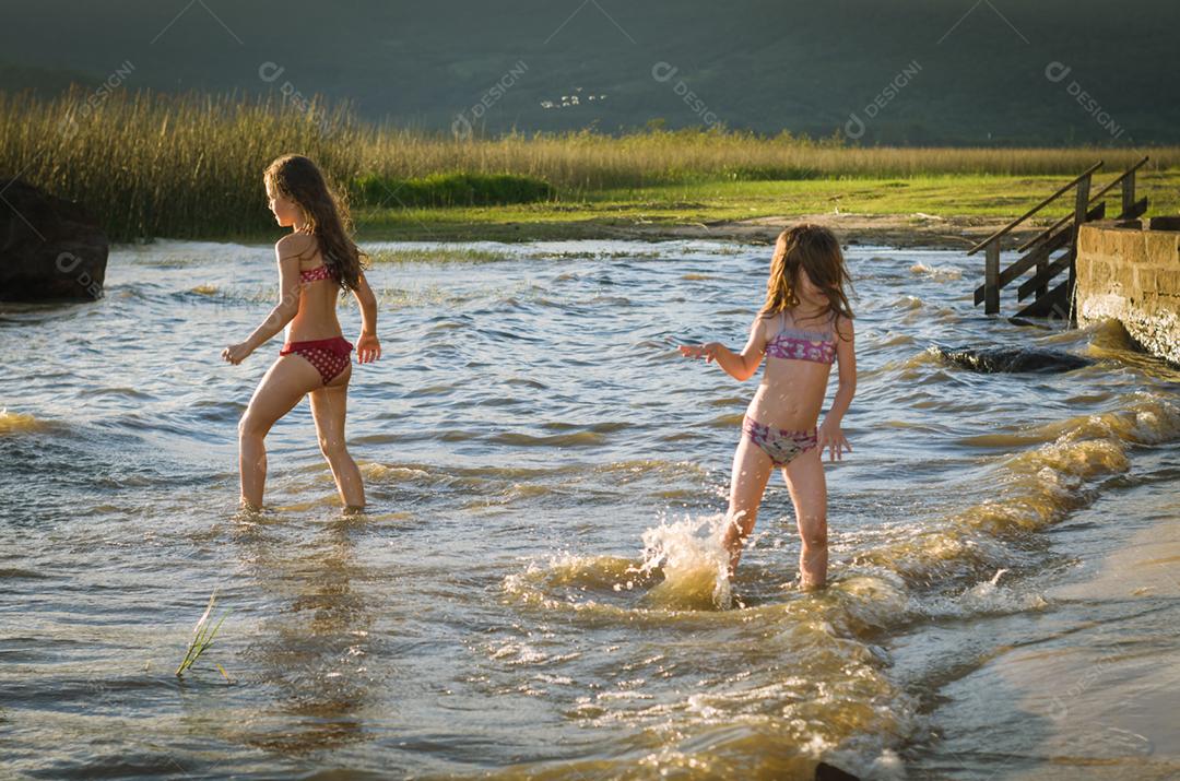 Lindas criança irmãs bricando sobre rio por do sol