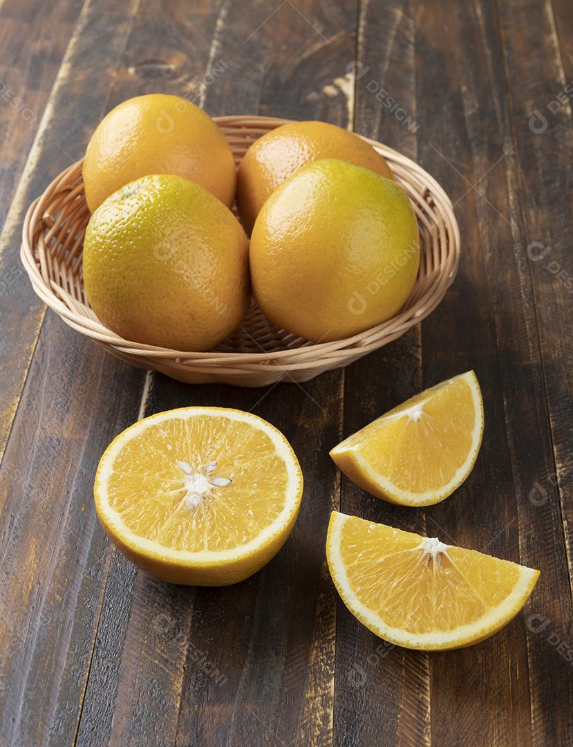 Laranjas em uma cesta com frutas cortadas sobre mesa de madeira