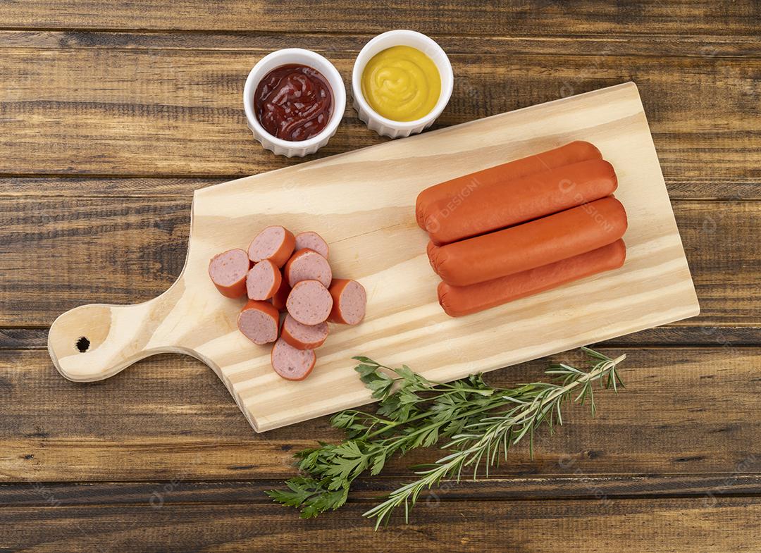 Salsichas e fatias sobre uma tábua de madeira com ketchup e mostarda