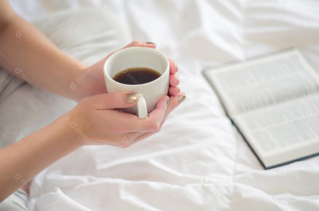 Mulher com pernas cruzadas, lendo livro e bebendo café. Visto