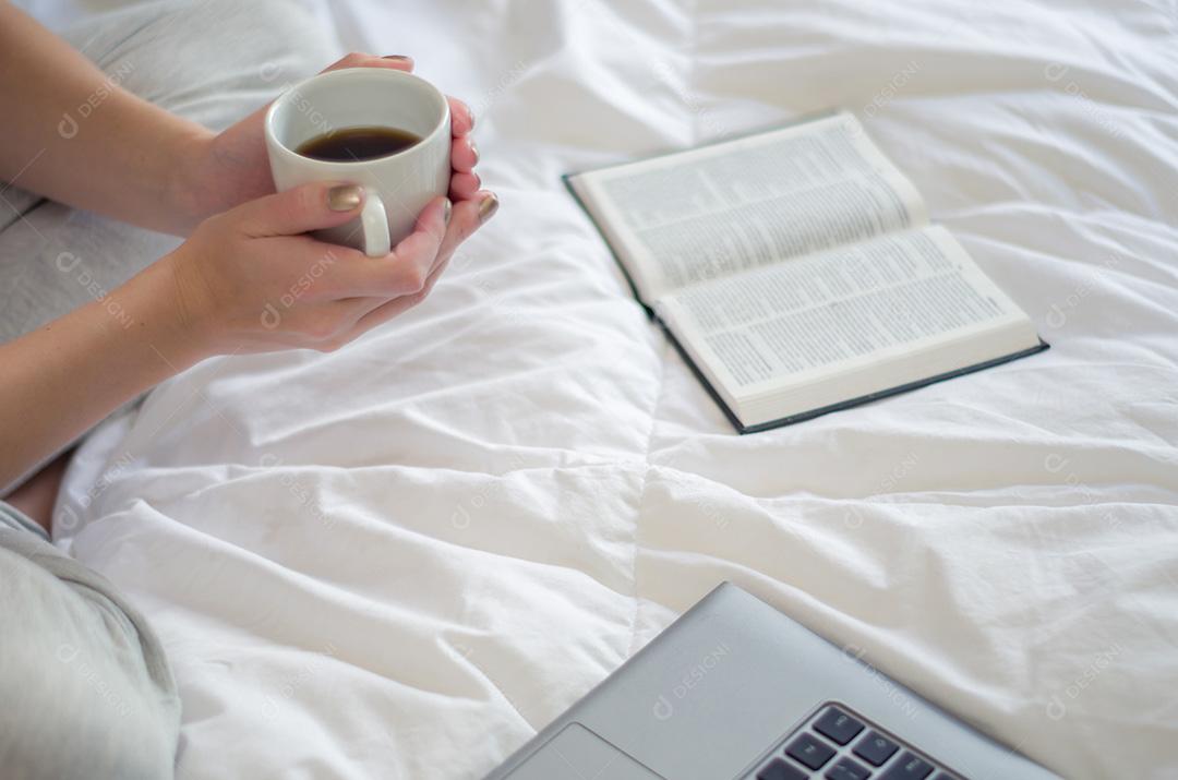 Mulher com pernas cruzadas, lendo livro e bebendo café. Visto