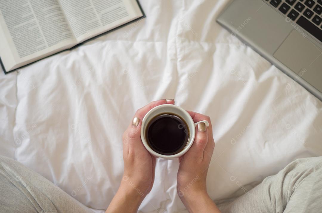 Mulher com pernas cruzadas, lendo livro e bebendo café, compu