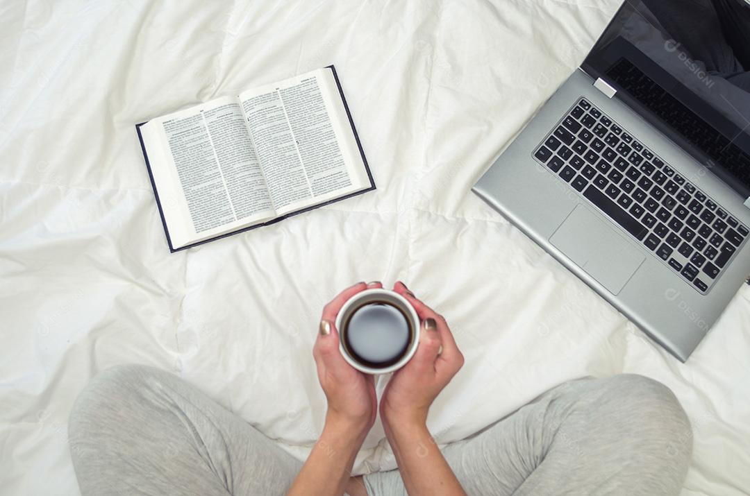 Mulher com pernas cruzadas, lendo livro e bebendo café, compu