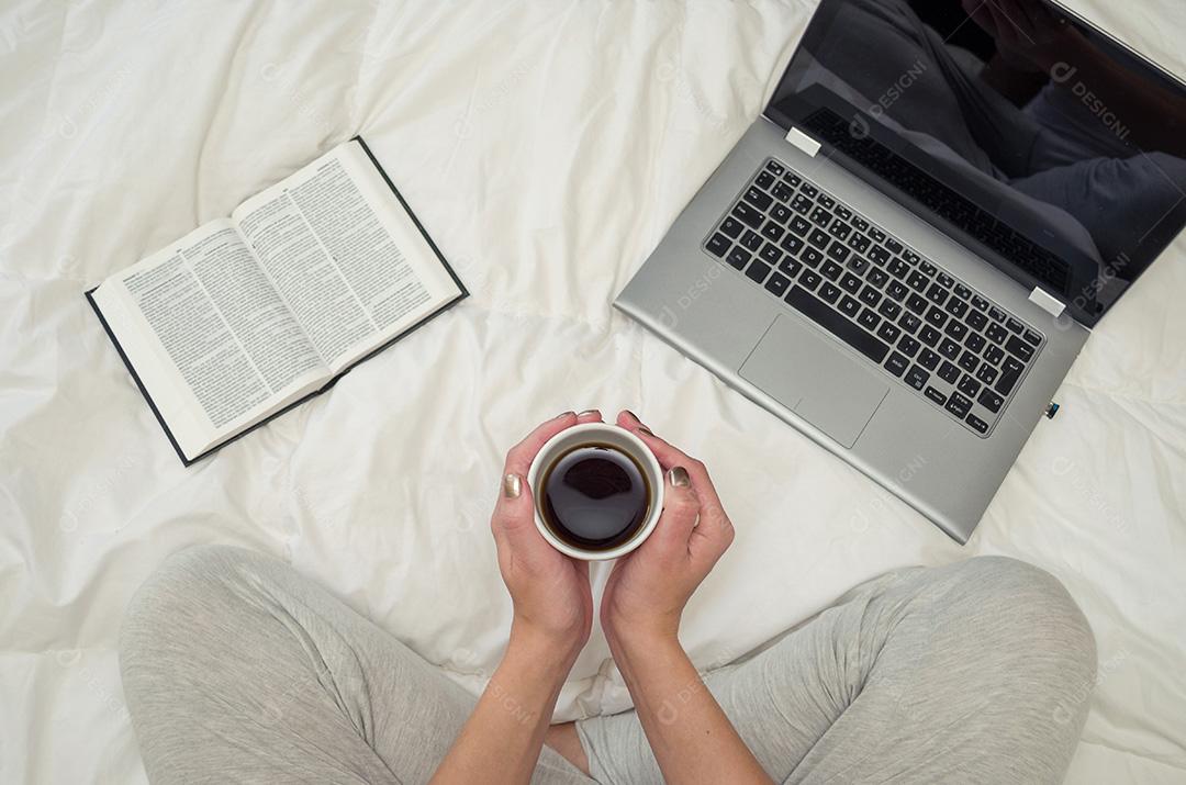 Mulher com pernas cruzadas, lendo livro e bebendo café, compu